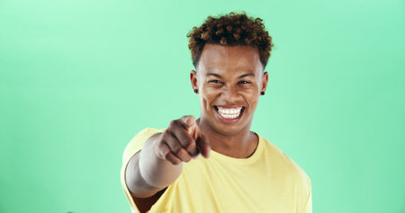 Happy, portrait or black man pointing to you on green background for choice in studio. Male person, model or smile with selection, choose or gesture for pick, decision or opportunity on mockup spaceの写真素材