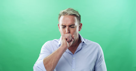 Coughing, sickness and virus with man in studio for allergies, influenza symptoms and illness. Fatigue, sinus congestion and healthcare with person on green background for infection, space and coldの写真素材