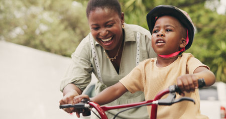 Support, teaching and boy on bicycle with mom on street of neighborhood for child development. African woman, smile or black kid with trust, help or single mother to learn how to ride bike outsideの写真素材