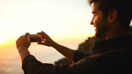 Man, hands and phone camera with sunset for picture, photography or capture moment in nature. Male person, hiker or travel with mobile smartphone or app for scenic view or memory of outdoor adventureの写真素材