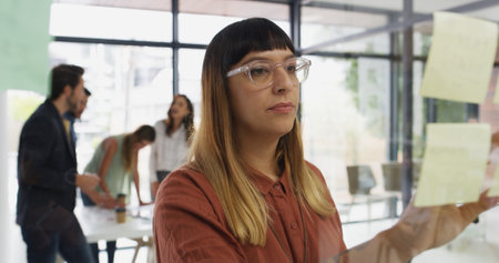Woman, sticky note and planning by window at office, idea or review for project management at startup. Person, paper and mindmap with glass, task or perspective with moodboard at creative agencyの写真素材