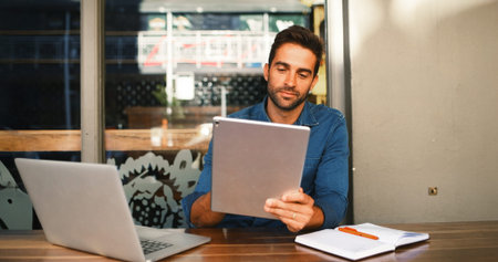 Cafe, man and reading on tablet for freelancer, article information or online blog for publication. Coffee shop, male person and content writer with laptop for remote work, newsletter or scroll emailの写真素材