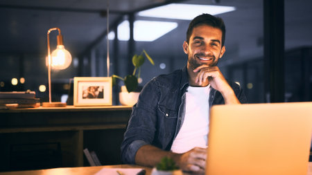 Office, night and businessman with laptop in portrait, proofreading and deadline for news article. Late, male person and journalist with smile for blog website, editing story and online publicationの写真素材