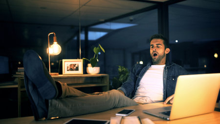 Laptop, yawn and tired businessman in night office for research, copywriting deadline or project. Creative worker, writer or editor with fatigue, burnout or exhausted for editing news article onlineの写真素材