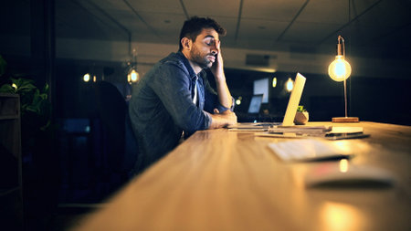 Laptop, tired and business man in night office for research, copywriting deadline or project. Creative worker, writer or editor with fatigue, burnout or exhausted for editing news article onlineの写真素材