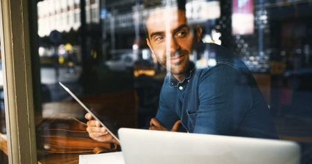 Coffee shop, thinking and man by window on tablet for project ideas, remote work and research. Cafe, inspiration and person on tech and laptop for website, online networking and report for freelanceの写真素材