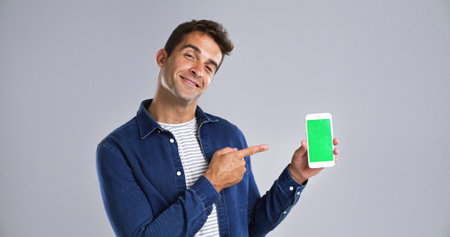 Man, portrait and phone pointing to green screen in studio for website, mockup space and white background. Student person, user or model with smile, smartphone or software app for university scheduleの写真素材