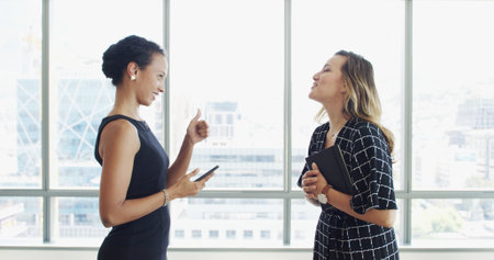 Business women, discussion and thumbs up with smile in lobby for agreement, deal or yes at company. People, partnership and phone with profile, sign or thank you for collaboration at insurance agencyの写真素材