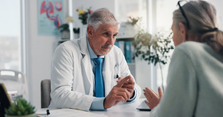 Doctor, mature woman and advice in clinic for medical services, consultation or opinion. People, symptoms and patient in conversation for appointment, checkup and healthcare with treatment discussionの写真素材