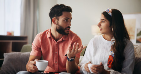 Couple, talk and coffee with question on sofa in home, communication and bonding in living room. People, man and woman with conversation for connection, relax and listen with tea cup at apartmentの写真素材