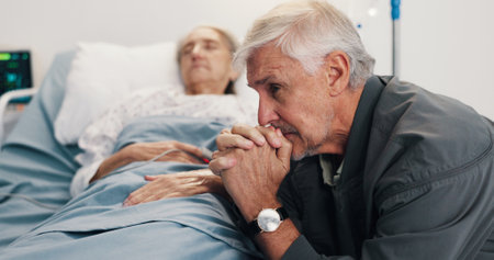 Elderly couple, sick and sad man with stress by hospital bed, cancer diagnosis and healthcare. Terminal illness, woman and clinic visitor with patient for hope, thinking and prayer for recoveryの写真素材