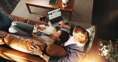 Laptop, phone and top view of couple on sofa for relax, chill and internet for bonding in home. Dating, relationship and man with woman on tech for social media, website and connection on weekendの写真素材