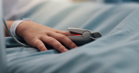 Hand, child and pulse oximeter on hospital bed to measure blood levels, monitor and recovery. Closeup, young patient and resting with medical machine, track oxygen and critical care from procedureの写真素材