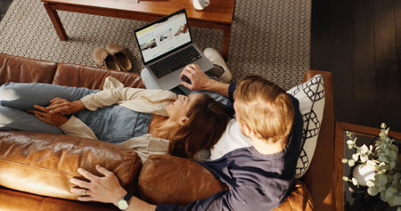 Laptop, relax or top view of couple in home to search for deal on accommodation or hotel booking. Screen, holiday or people on couch together for bonding, travel options or resort homepage for reviewの写真素材
