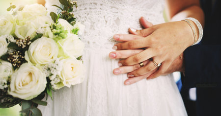 Couple, holding hands or marriage with flowers at wedding for commitment, love or romance at ceremony. Closeup, bride or groom with bouquet, loyalty or touch for trust, support or engagement togetherの写真素材
