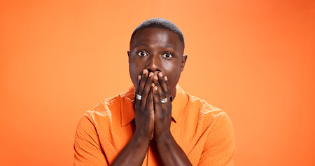 Man, reaction and surprised by news, portrait or expression for gossip, orange background or studio. Mockup space, black person and shocked by rumor, wow and listening to announcement in Kenyaの写真素材