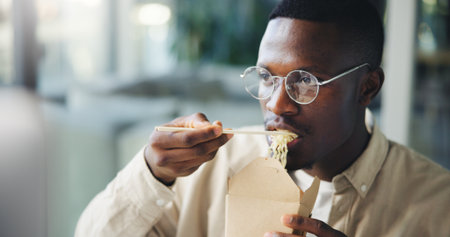 Business, black man or eating by computer in office for working break, reading article and hungry. Media agency, journalist and chinese takeout for lunch, submission deadline and proofreading blogの写真素材