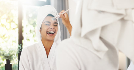 Laugh, brush and makeup with woman and mirror for foundation application, beauty and tools. Facial, smile and cosmetics with reflection of person in bathroom of home for glow, product and blushの写真素材