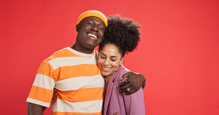 Hug, smile and black couple in studio, love and bonding together on red background. Romance, embrace and man with woman, relationship and support with happiness, trust and commitment with marriageの写真素材