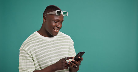 Phone, smile and black man in studio for social media, text message or reading fashion blog. Mobile,...