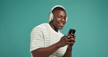 Headphones, smile and black man in studio, cellphone or listening to music on green background....