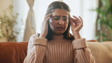 Woman, pain and headache of stress on sofa for financial crisis, overwhelmed or mental health. Glasses, person or tension migraine in home for wrong prescription, overthinking or dizzy for bankruptcyの写真素材