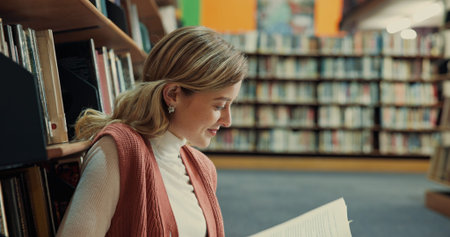 Student, textbook and girl in library with reading, assignment or thesis research by bookshelf....