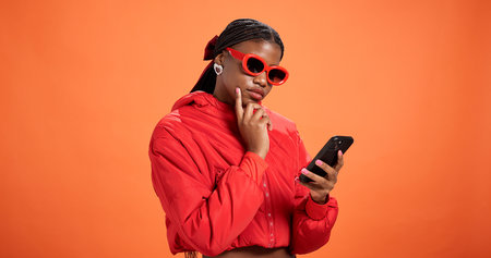 Woman, phone and texting in studio with thinking, chat and reading post on app on orange background...