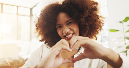 Hands in heart, home and portrait of black woman with smile for relaxing, happy and social media. Living room, apartment and face of person with gesture, emoji and sign for love, romance and flirtの写真素材
