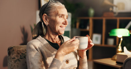 Senior woman, tea and thinking on sofa with happy memory, daydreaming and peaceful in retirement. Relax, elderly person and smile with warm beverage in home for reflection, remember and wonderingの写真素材