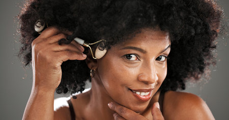 Woman, skincare and jade roller in studio with facial routine, beauty and anti aging by background. African person, portrait and tools with massage, circulation and product for results in Nigeriaの写真素材