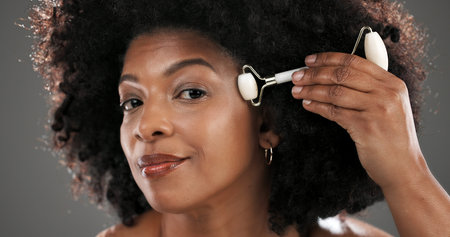 Woman, quartz roller or cosmetics in studio for facial routine, stone or antiaging by gray background. Black person, beauty or portrait for massage tools, circulation or skincare for results in Kenyaの写真素材