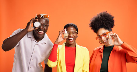 People, happy and products in studio for skincare, comparison or choice for dermatology. African friends, laugh or lotion container on orange background for cosmetic opinion, serum or beauty portraitの写真素材