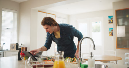 Home, reading or man on tablet for cooking recipe method, lunch or learning guide in kitchen. Online tutorial, technology or chef on touchscreen with ingredients instruction, food or meal prep stepsの写真素材