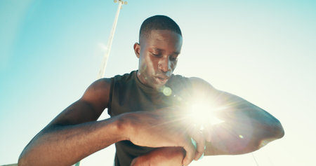 Black man, runner and smart watch in city for exercise, stats or break with low angle for training. Person, athlete and heart rate with timer, stopwatch and app with sweat, workout and tired in Kenyaの写真素材