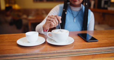 Hands, drink and customer stir coffee on table for beverage, espresso and preparation. Cup, latte and woman with spoon for mixing morning cappuccino with fresh cream or foam in restaurant to relaxの写真素材
