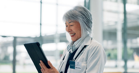 Healthcare, doctor and Asian woman in hospital, tablet and email for medical report. Mature person, happy or professional in clinic, tech and app for schedule, research mission or positive resultsの写真素材