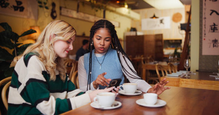 Coffee shop, friends and women with phone for relax, bonding or post review on social media. Mobile, conversation and girls together in restaurant for internet gossip, blog or show story for hangoutの写真素材