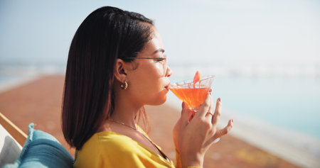 Swimming pool, relax and woman with cocktail, vacation and travel with weekend break. Outdoor, tourism and person with alcohol, drinking and summer holiday with wellness, resort and luxury hotelの写真素材