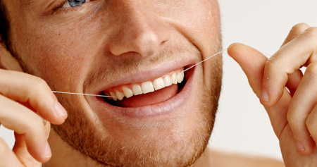 Oral health, floss and man in studio with hygiene, wellness and mouth routine in morning. Dental care, fresh breath and person with string for cleaning teeth with plaque removal by white background.の写真素材