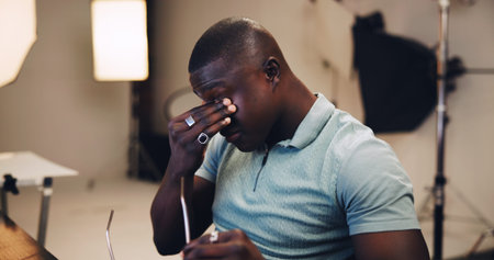 Frustrated, black man and headache with eye strain in production studio for overworked or stress....