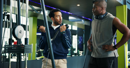 Personal trainer, teaching and man with rope machine for advice, exercise and coaching. Explain, biceps and athlete in training with instructor or gym equipment, muscle and workout for fitness tipsの写真素材