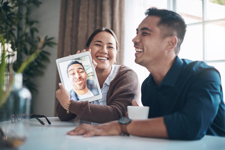 Couple of friends, video call and tablet screen with people laughing in living room of home together. Face, funny or humor with happy young man and woman in apartment for communication or online chatの写真素材