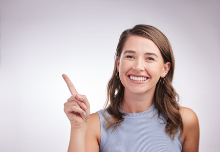 Pointing, smile and portrait of woman in studio with mockup space for advertising, promotion or marketing. Happy, decision and female person with presentation or choosing gesture by white background.の写真素材
