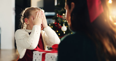 Girl, mom and cover eyes for Christmas present, tree and surprise with love, bonding and festive holiday. Child, mother and daughter with box, package and gift with xmas celebration at family houseの写真素材