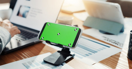 Phone, green screen and business person in office for research, finance report and performance. Mockup space, hand and laptop for financial planning, tax information and investment proposal graphsの写真素材