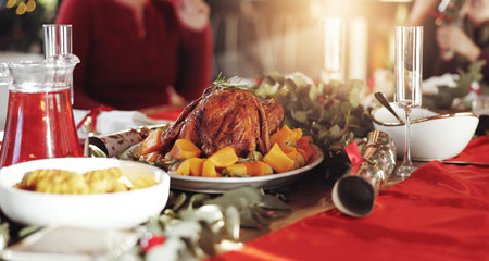 Food, dinner table and christmas meal with family for thanksgiving or festive celebration in home. People, chicken and decor with dinning setting for eating, bonding or december holiday togetherの写真素材