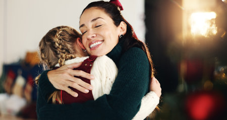 Christmas, hug and smile of mother with daughter in living room of home for celebration together. December, festive or winter with happy single parent and girl child embracing in apartment for loveの写真素材