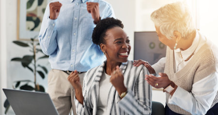 Celebration, happy and business people with laptop in office for good news, achievement or target. Fist pump, job promotion and businesswoman with support from team for goal together in workplace.の写真素材