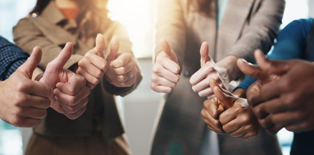 Business people, hands or teamwork with thumbs up in office for diversity, inclusion or feedback. Group, employees or gesture with like emoji, yes sign or OK for work cohesion, well done or agreementの写真素材